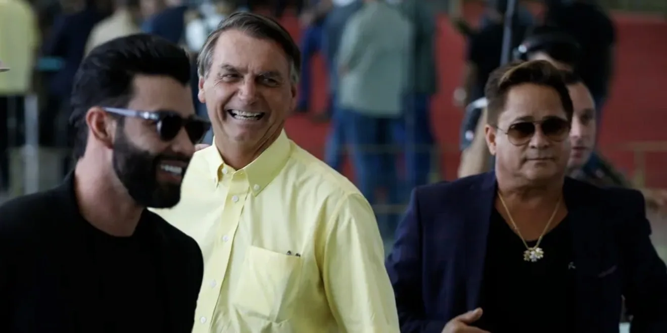 Imagem do cantor Leonardo sorrindo com microfone na mão, ao lado de foto de Flávio Bolsonaro, com fundo de palco sertanejo e elementos de bandeira do Brasil, simbolizando o posicio